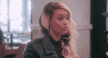 a woman wearing a leather jacket and earrings is sitting at a table looking at a cell phone .