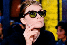 a woman wearing sunglasses holds a cigarette to her face