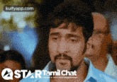 a man with a beard is standing in front of a star tamil chat sign