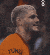 a close up of a man wearing an orange shirt with yuns written on it
