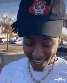 a man wearing a hat and a chain is smiling while standing in a parking lot .