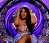 a woman wearing a crown is sitting in a chair with a purple background