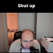 a man with a beard is sitting in front of a microphone with the word shut up above him