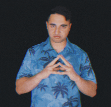 a man in a blue shirt with palm trees on it making a triangle with his hands