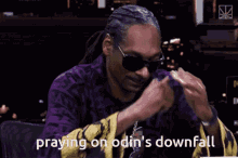 snoop dogg is praying on odin 's downfall with his hands folded