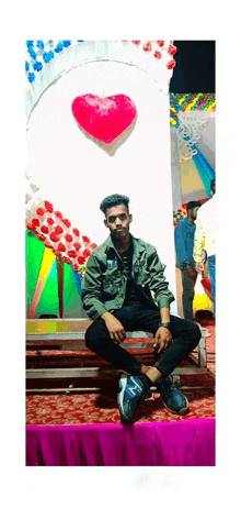 a man is sitting on a bench in front of a heart shaped balloon .
