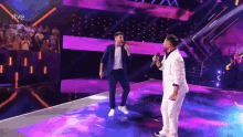 two men singing into microphones on a stage with a rtve logo behind them