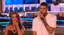 a man and a woman are standing next to each other and covering their mouths .