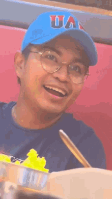 a man wearing a blue ua hat and glasses is smiling