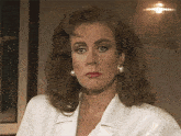 a woman wearing pearl earrings and a white jacket