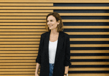 a woman wearing a black jacket and a white shirt is standing in front of a wooden wall