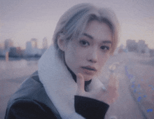 a young man with blonde hair and a white fur collar is standing in front of a city .