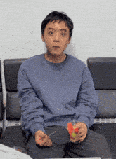 a man in a blue sweater is sitting on a couch holding a glass of fruit