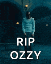 a man in a white sweater is walking in a dark room with the words rip ozzy written above him .