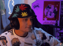 a man wearing a hat with marijuana leaves on it sits in front of a sign that says nuka cola