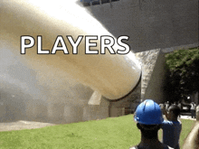 a man wearing a blue hard hat is standing in front of a large pipe that says players on it .