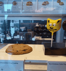 a chocolate chip cookie and a bumblebee cake pop are on display in a store