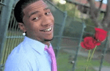 a man in a blue shirt and pink tie is holding a red rose .