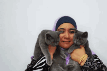 a woman in a hijab is holding two gray cats