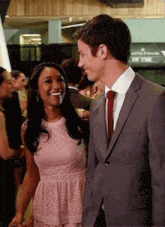 a man in a suit and tie is standing next to a woman in a pink dress and holding her hand .