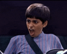 a young boy in a striped shirt is making a surprised face while sitting in a car .
