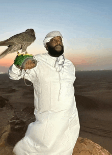 a man in a white robe holds a falcon on his arm