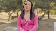 a woman in a pink dress is sitting on a rock in front of trees