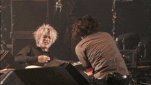 a man in a black shirt with a star on it is playing a guitar with another man
