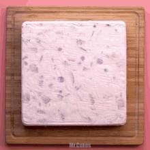 a square piece of ice cream on a wooden cutting board with the words mr.cakes below it