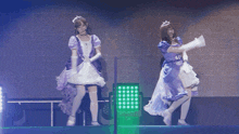 two women in purple and white dresses are dancing on stage