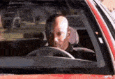 a bald man is driving a red car with the word extremeblitz on the windshield