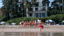 a group of people running on a beach with a large house in the background