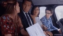 a group of people are sitting in a car with a man holding a check .