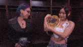 two women are standing in a locker room one is holding a wrestling championship belt