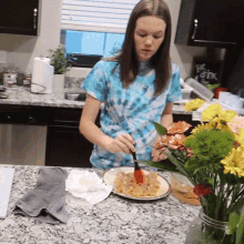 a woman in a blue tie dye shirt is preparing food