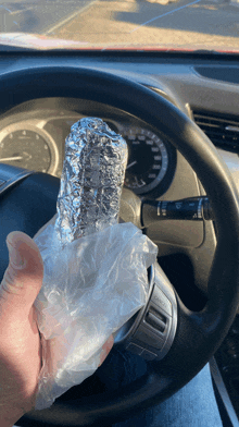 a person in a car holding a plastic bag with a burrito in it