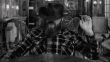 a man with a beard is wearing a plaid shirt and a cowboy hat