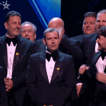 a group of men in tuxedos and bow ties are standing on a stage with a star in the background