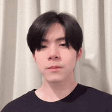 a young man in a black shirt is standing in front of a white curtain and looking at the camera .