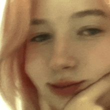 a close up of a woman 's face with pink hair and a hand on her chin .