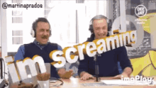 two men sitting at a table with a sign that says screaming
