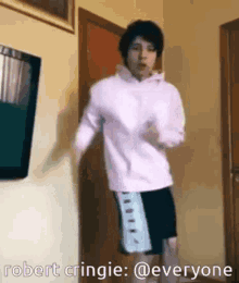 a person in a pink hoodie and shorts is dancing in a room .