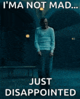 a man is standing in a dark room with the words `` i 'm not mad ... just disappointed '' written on it .