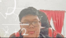 a young man wearing glasses is sitting in front of a chalkboard with mathematical equations written on it .