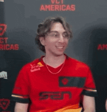 a man in a red shirt is making a funny face while wearing glasses .