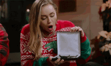 a woman in a red and green sweater opens a box