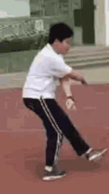 a man in a white shirt and black pants is standing on a track holding a tennis racquet .