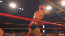 a wrestler in a red outfit is jumping over a red rope