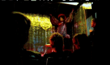 a blurry picture of a man standing in front of a crowd in a dark room with a green shirt on
