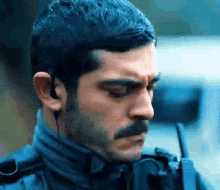 a man with a mustache is wearing earbuds and a walkie talkie